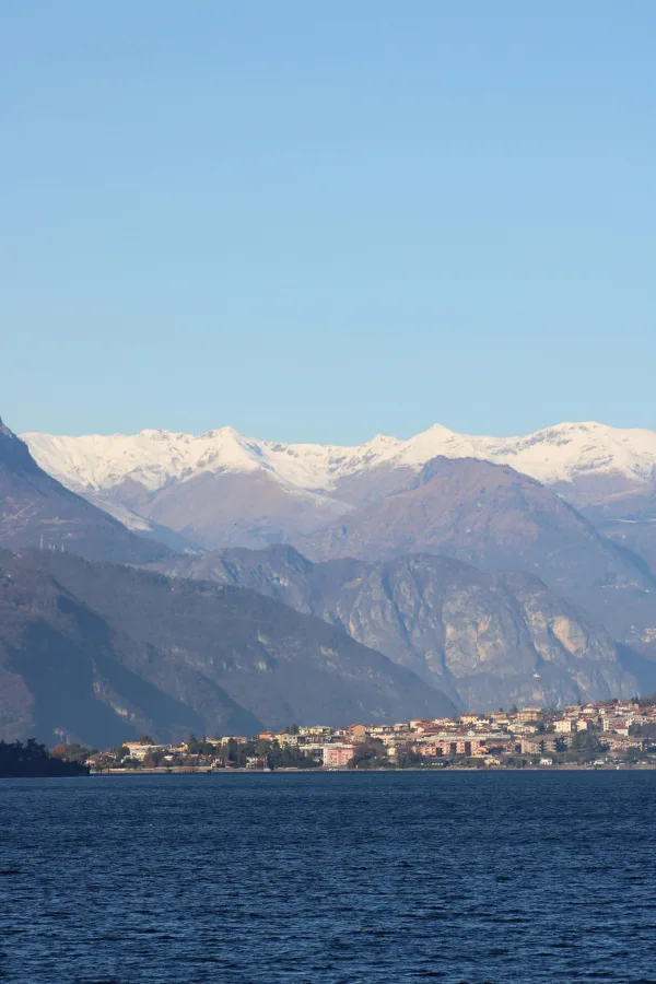 Village au bord d’un lac avec montagnes enneigées sous un ciel bleu