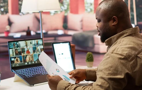 Homme en visioconférence analysant des documents en télétravail