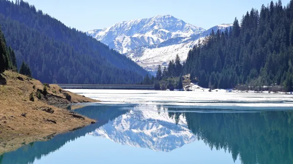 Lac de montagne avec reflet des sommets enneigés dans une vallée alpine