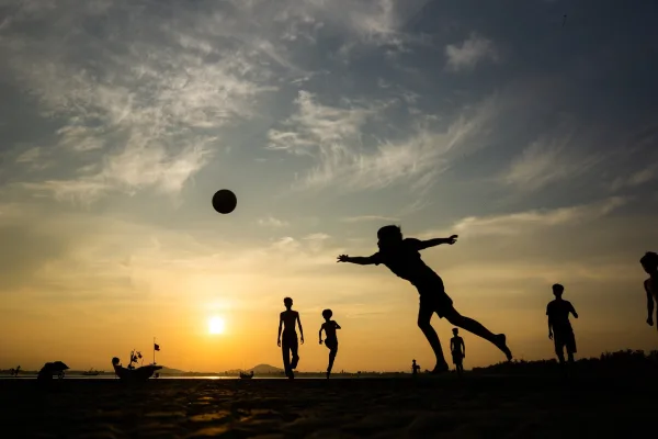 Enfants jouant au football sur la plage au coucher du soleil
