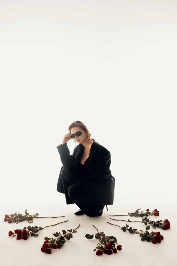 Portrait artistique d’une femme en tenue noire entourée de roses rouges dans un studio minimaliste