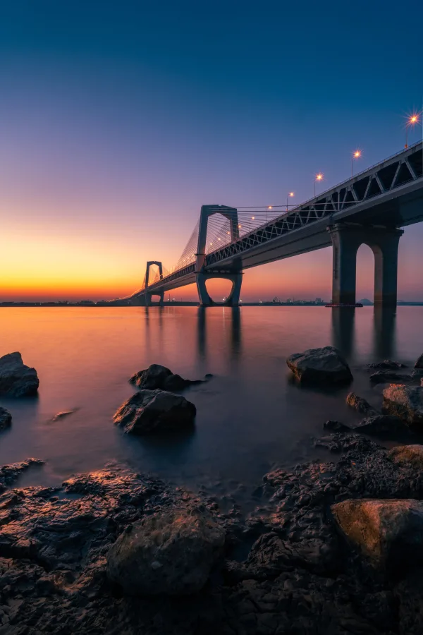 Pont suspendu illuminé au coucher du soleil au-dessus de l'eau calme