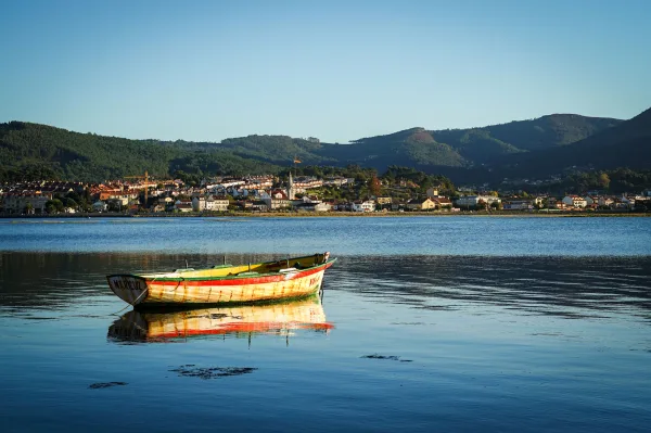 Barque colorée sur une eau calme face à un village côtier et des collines verdoyantes