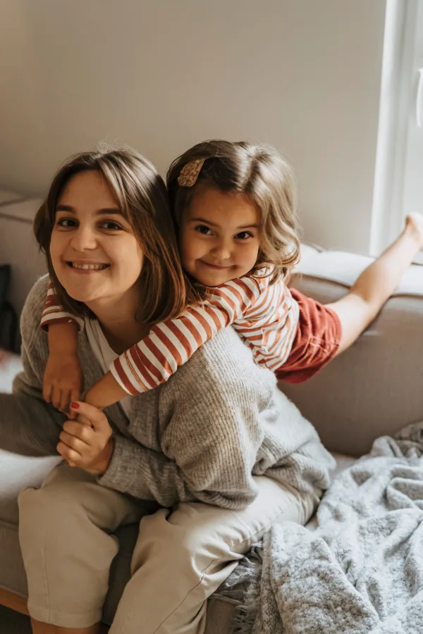 Mère et fille souriantes enlacées sur un canapé à la maison