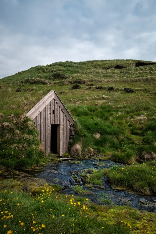 Petite cabane en bois près d’un ruisseau dans une prairie verdoyante
