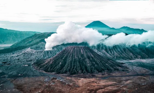 Volcan actif dégageant un panache de fumée dans un paysage montagneux