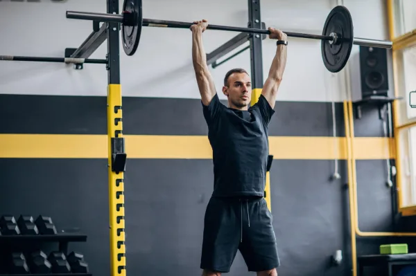 Athlète réalisant un développé militaire avec barre en salle de sport