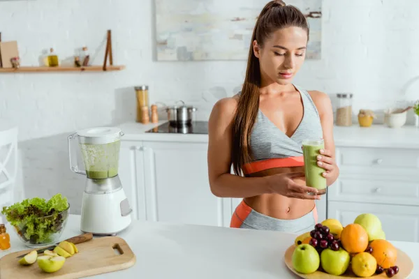 Femme sportive buvant un smoothie vert healthy dans une cuisine moderne