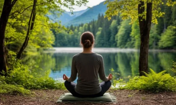 Femme en méditation au bord d'un lac entouré par la nature