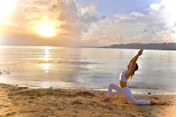 Femme pratiquant le yoga sur une plage au lever du soleil