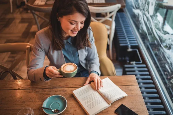 Femme lisant un livre dans un café avec une tasse de café, symbole d'apprentissage et de détente