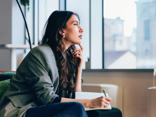 Femme réfléchissant près d'une fenêtre, symbole d'introspection, de confiance en soi et de développement personnel