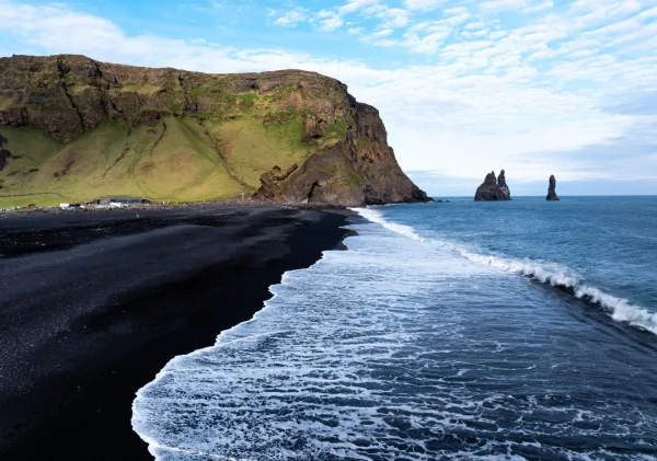 Plage de sable noir volcanique bordée de falaises et de formations rocheuses en Islande