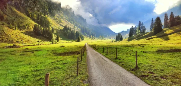 Route de montagne à travers une vallée verdoyante sous un ciel spectaculaire