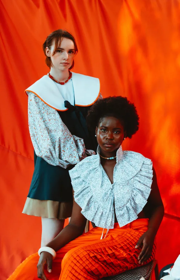Portrait de deux femmes en tenues de haute couture devant un fond rouge artistique