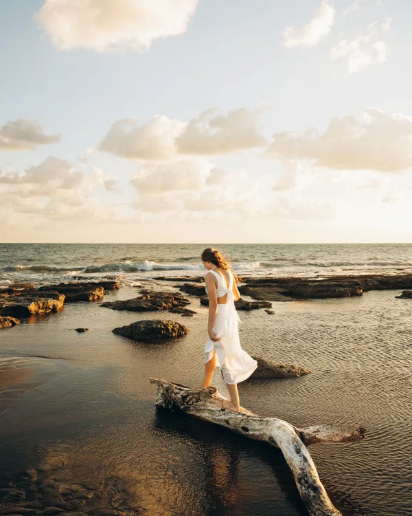 Femme marchant sur un tronc d'arbre au bord de la mer au coucher du soleil